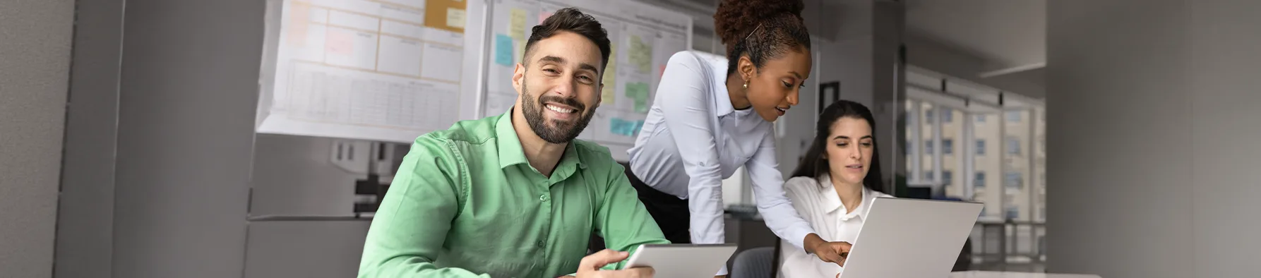 Grupo de profissionais trabalha em conjunto em um escritório moderno, utilizando notebook e tablet para elaborar uma proposta comercial estratégica.
