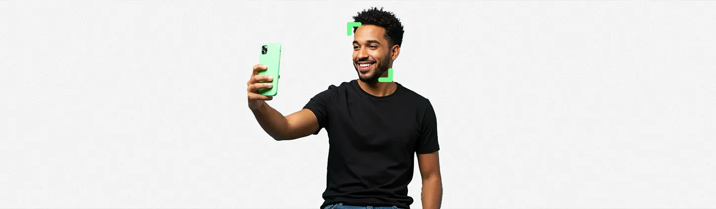 Um homem sorridente segura um smartphone com a câmera frontal ativada, pronto para assinar documentos com selfie.