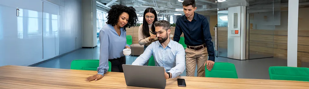 Equipe colaborando em laptop em escritório moderno, discutindo o que é pegada de carbono e como fazer o cálculo de redução.