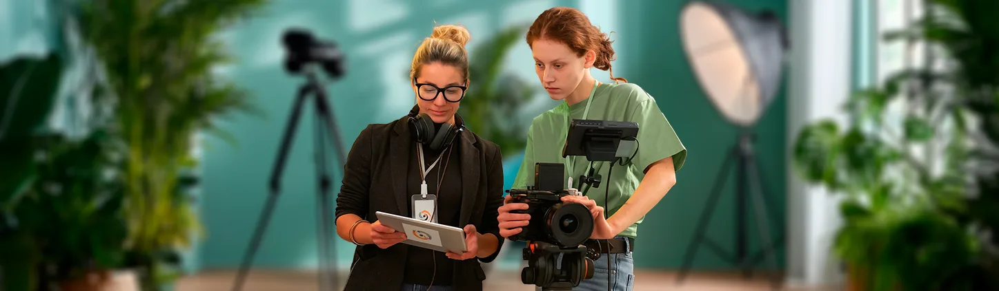 Duas mulheres, uma com um tablet e outra com uma câmera de vídeo profissional, trabalham juntas em um set de filmagem. A imagem pode representar o processo de obtenção de uma Autorização de uso de imagem de forma digital, agilizando as formalidades legais em um ambiente de produção.