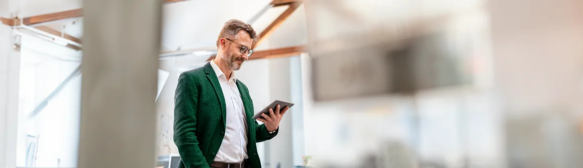 Um homem sorridente está segurando um tablet. A imagem demonstra a agilidade e segurança da tecnologia para a verificação de identidade com IA.