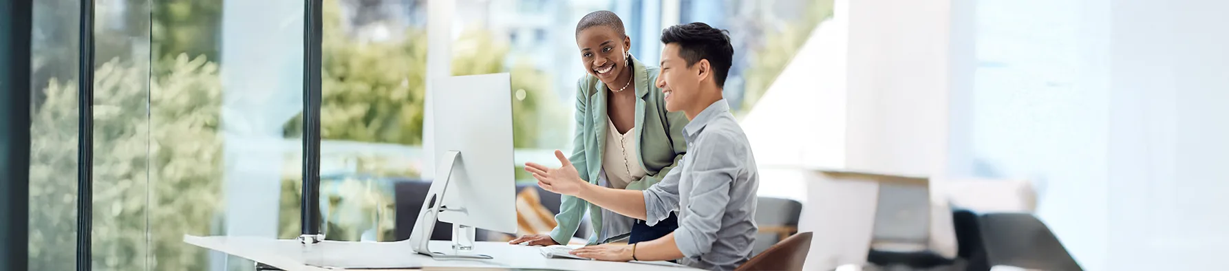 Dois colegas sorriem enquanto colaboram em um monitor de computador, ilustrando a comunicação e o trabalho em equipe essenciais para uma eficaz gestão de mudança.