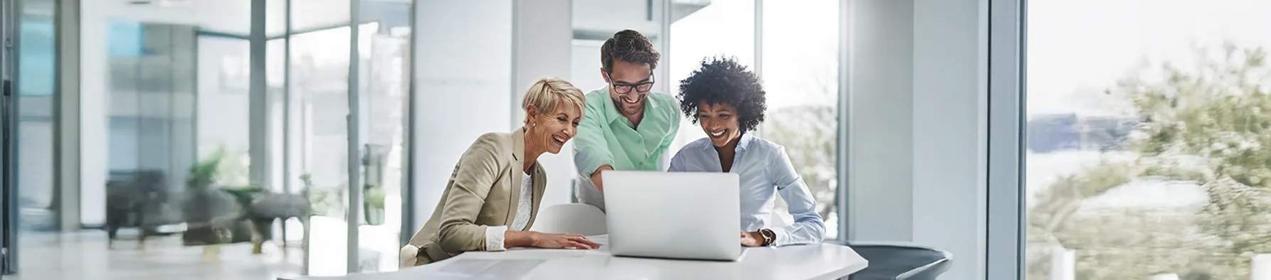 Três colegas sorridentes colaboram em um laptop, analisando dados e buscando estratégias para a otimização de LTV (Lifetime Value) e o crescimento do negócio.