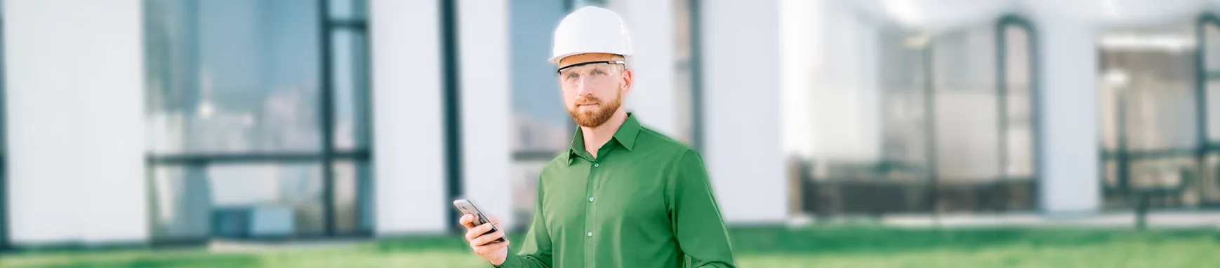 Engenheiro de capacete utiliza smartphone para realizar assinatura digital no setor de energia e saneamento em frente a um edifício.