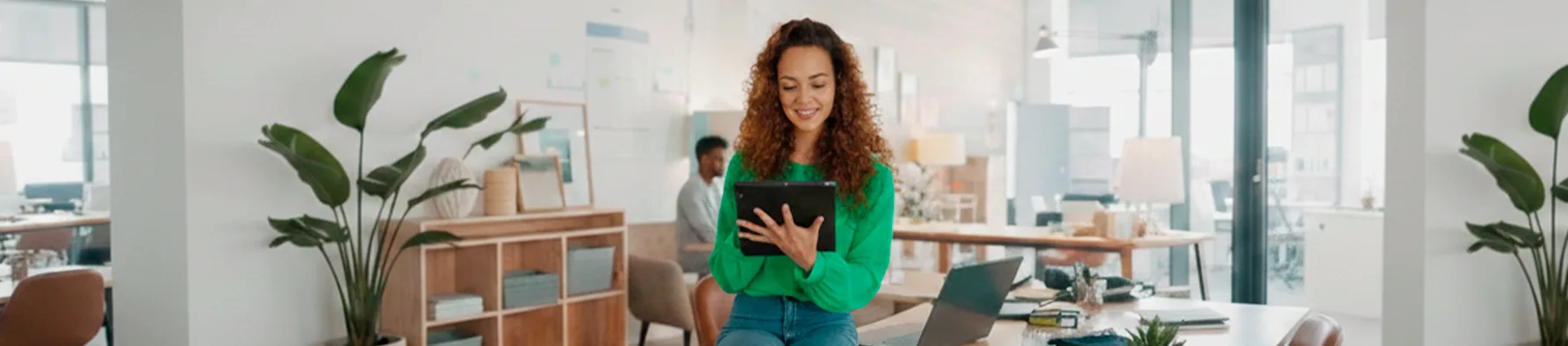 Mulher sorridente utiliza tablet em escritório moderno, destacando a agilidade da assinatura digital confiável para contratos e documentos.