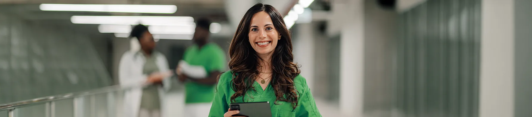 Profissional da saúde sorridente segura um tablet em um corredor hospitalar, exemplificando a eficiência da gestão de documentos na saúde.