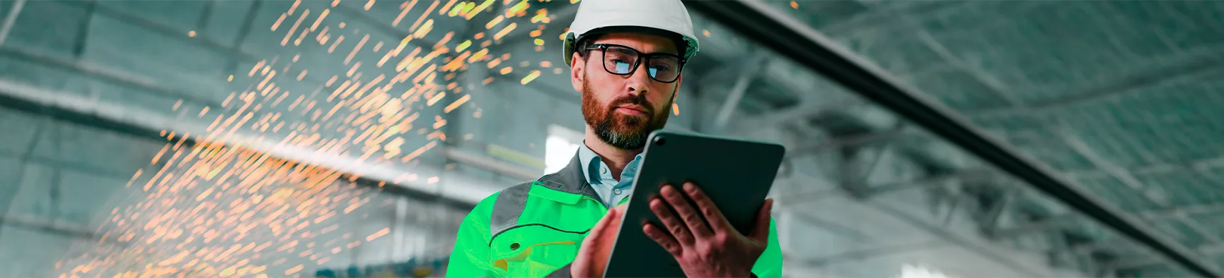 Profissional de engenharia usa tablet em um galpão fabril com faíscas ao fundo, demonstrando a aplicação prática da assinatura eletrônica no setor industrial.