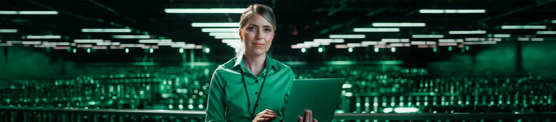 Profissional de TI com laptop em um vasto data center de luzes verdes, simbolizando a gestão de contratos de TI.