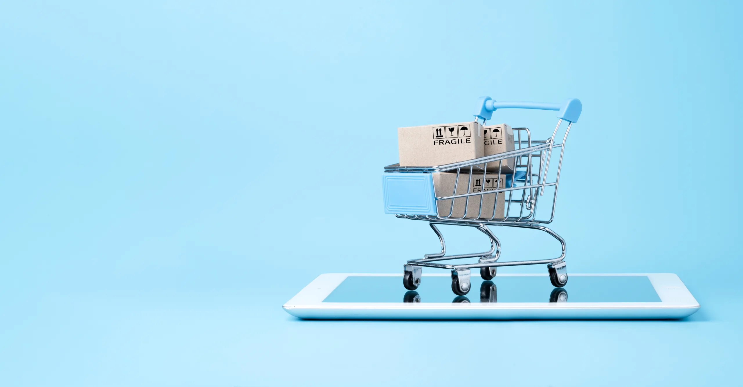 Miniatura de carrinho de compras com caixas sobre um tablet, representando a assinatura eletrônica para e-commerce.